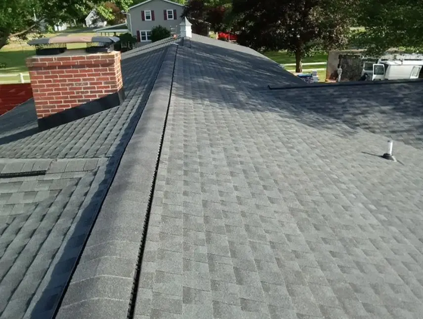 Close-up view of a newly installed gray shingle roof with a brick chimney and a clear sky in the background.