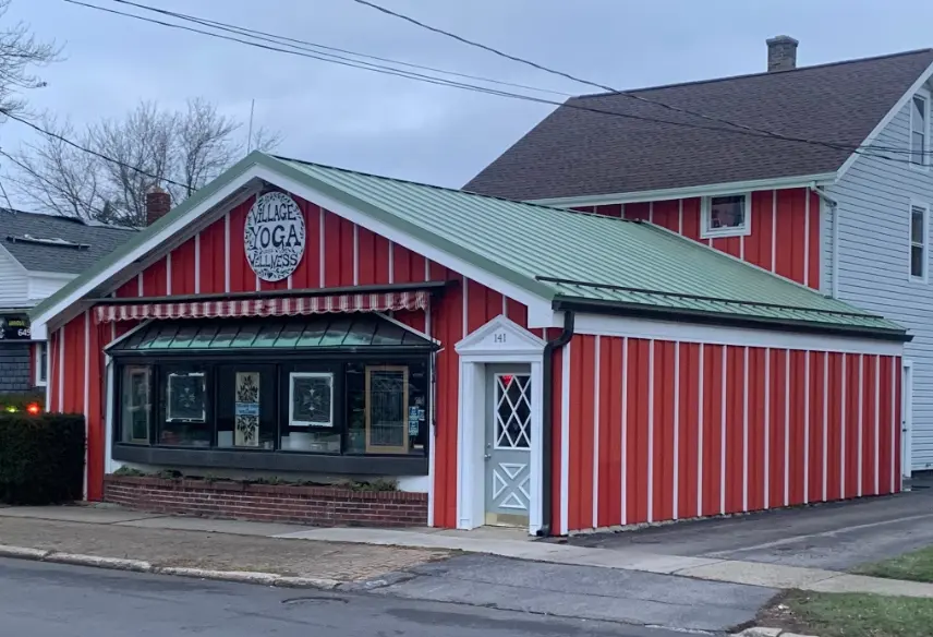 Red and white striped Village Yoga Wellness building with a green metal roof in a residential neighborhood.